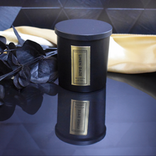 Load image into Gallery viewer, Matte black Linen Daze candle with lid on, showcasing an elegant gold foil label, styled with modern black botanicals and rich golden backdrop.