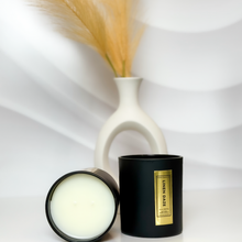 Load image into Gallery viewer, Handcrafted Linen Daze candle duo featuring creamy soy wax and matte black jars with gold foil labels, styled against a wave-textured white backdrop with fresh eucalyptus in a modern vase.