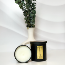Load image into Gallery viewer, Matte black Linen Daze candle set with lid on and one candle tipped to reveal smooth white soy wax, styled in front of a sculptural white vase filled with eucalyptus for a modern, minimalist vibe.