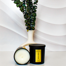 Load image into Gallery viewer, Matte black Linen Daze candle set with lid on and one candle tipped to reveal smooth white soy wax, styled in front of a sculptural white vase filled with eucalyptus for a modern, minimalist vibe.