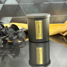 Load image into Gallery viewer, Linen Daze candle with matte black lid on, styled with deep black eucalyptus and soft gold fabric, capturing a cozy and refined home ambiance.