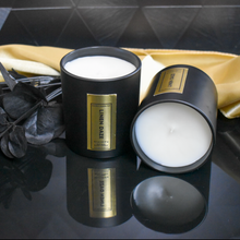 Load image into Gallery viewer, uxury Linen Daze candle in 8.5 oz matte black jar with gold foil label, reflected on a glossy black surface with dried eucalyptus and a golden accent cloth in the background.
