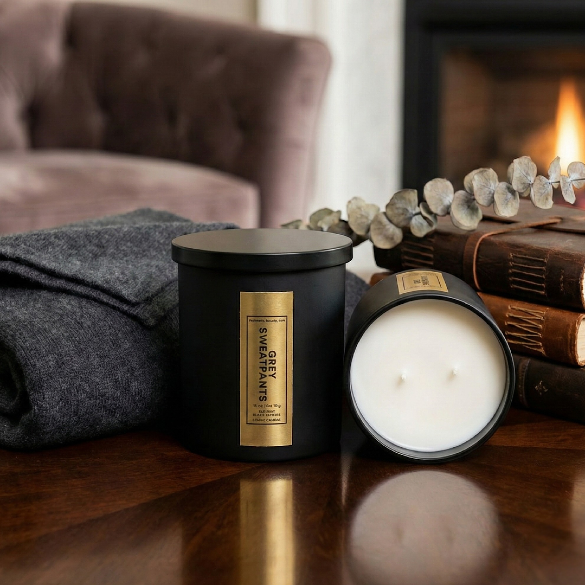 Black candle with gold label on a wooden surface, with a cozy indoor setting featuring a fireplace and books.