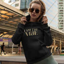 Load image into Gallery viewer, Woman wearing a black hoodie with 'I AM THE VIBE' text in an urban setting
