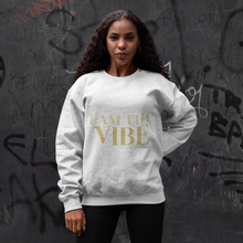 Load image into Gallery viewer, Woman wearing a white sweatshirt with 'I AM THE VIBE' text in gold against a graffitied wall.
