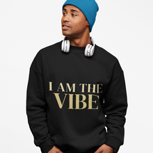 Load image into Gallery viewer, Person wearing a black sweatshirt with 'I AM THE VIBE' text, blue beanie, and white headphones on a light gray background
