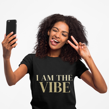 Load image into Gallery viewer, Woman wearing a black t-shirt with a 'I AM THE VIBE' design, holding a phone and making a peace sign.
