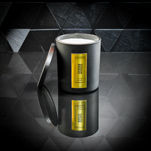 Load image into Gallery viewer, A sleek black candle jar labeled “Ocean Breeze” with a reflective gold foil label, displayed on a glossy black tiled surface. The candle lid is propped open, revealing the white wax inside, and the label reads “Kandie’s Scents, LLC” with minimalistic luxury branding.
