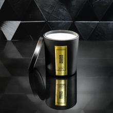 Load image into Gallery viewer, A sleek black candle jar labeled “Ocean Breeze” with a reflective gold foil label, displayed on a glossy black tiled surface. The candle lid is propped open, revealing the white wax inside, and the label reads “Kandie’s Scents, LLC” with minimalistic luxury branding.
