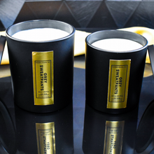 Load image into Gallery viewer, Two open Grey Sweatpants candles in black jars with vertical gold labels are displayed on a reflective background. The black and gold background create a moody, upscale vibe.
