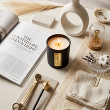 Load image into Gallery viewer, Candle with a label on a table with a magazine and decorative items
