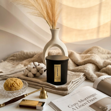 Load image into Gallery viewer, Candle with a label, vase with dried grasses, and other decorative items on a surface.
