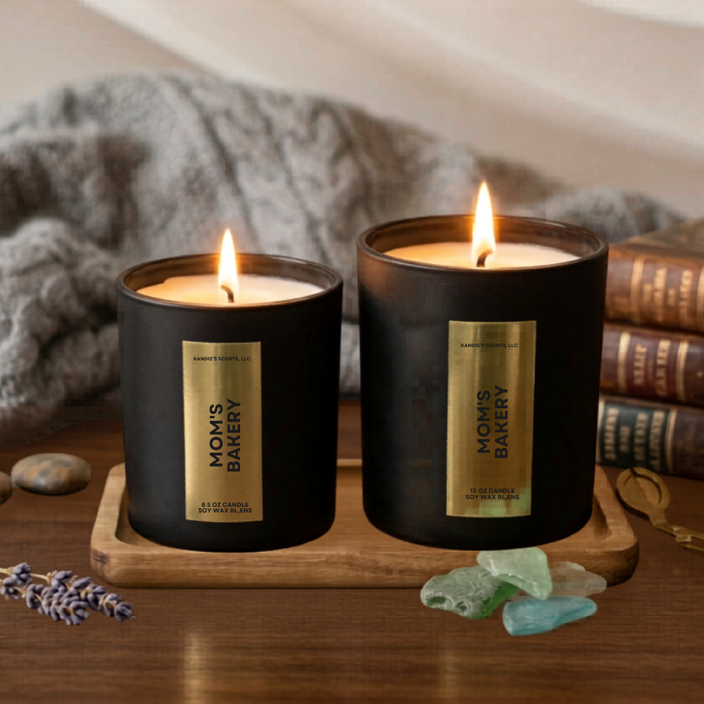 Two lit candles from 'Mom's Bakery' on a wooden tray with books and decorative stones in the background.