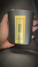 Load and play video in Gallery viewer, A close-up video of an 8.5 oz Ocean Breeze candle held in one hand and gently rotated to highlight its elegant gold foil label. The candle is housed in a matte black jar, and the reflective label catches the light, showcasing the luxury and craftsmanship of Kandie’s Scents’ signature scent.
