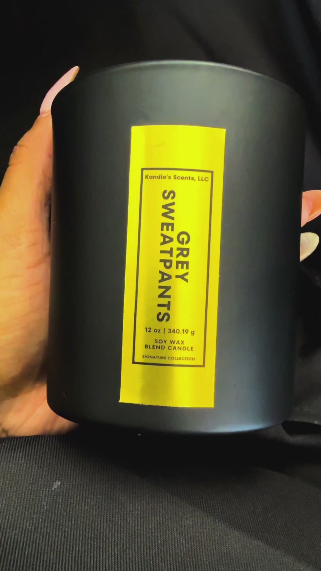A slow-turn video of the 12 oz Grey Sweatpants candle, cradled in one hand. The matte black jar with its tall, vertical gold foil label shimmers as it’s rotated, revealing the sleek, upscale branding of Kandie’s Scents. This premium candle embodies bold simplicity and timeless luxury.
